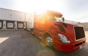 Red semi-truck parked at warehouse loading docks, representing Arizona freight brokerage services for shippers needing reliable carrier capacity.