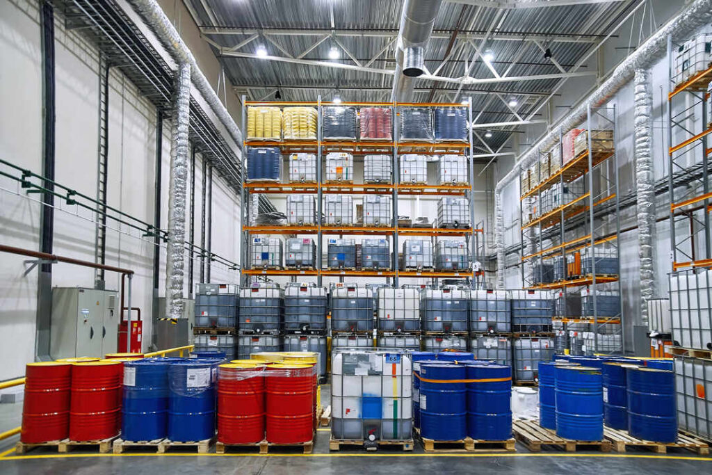 Organized hazmat storage warehouse with labeled drums and IBC totes
