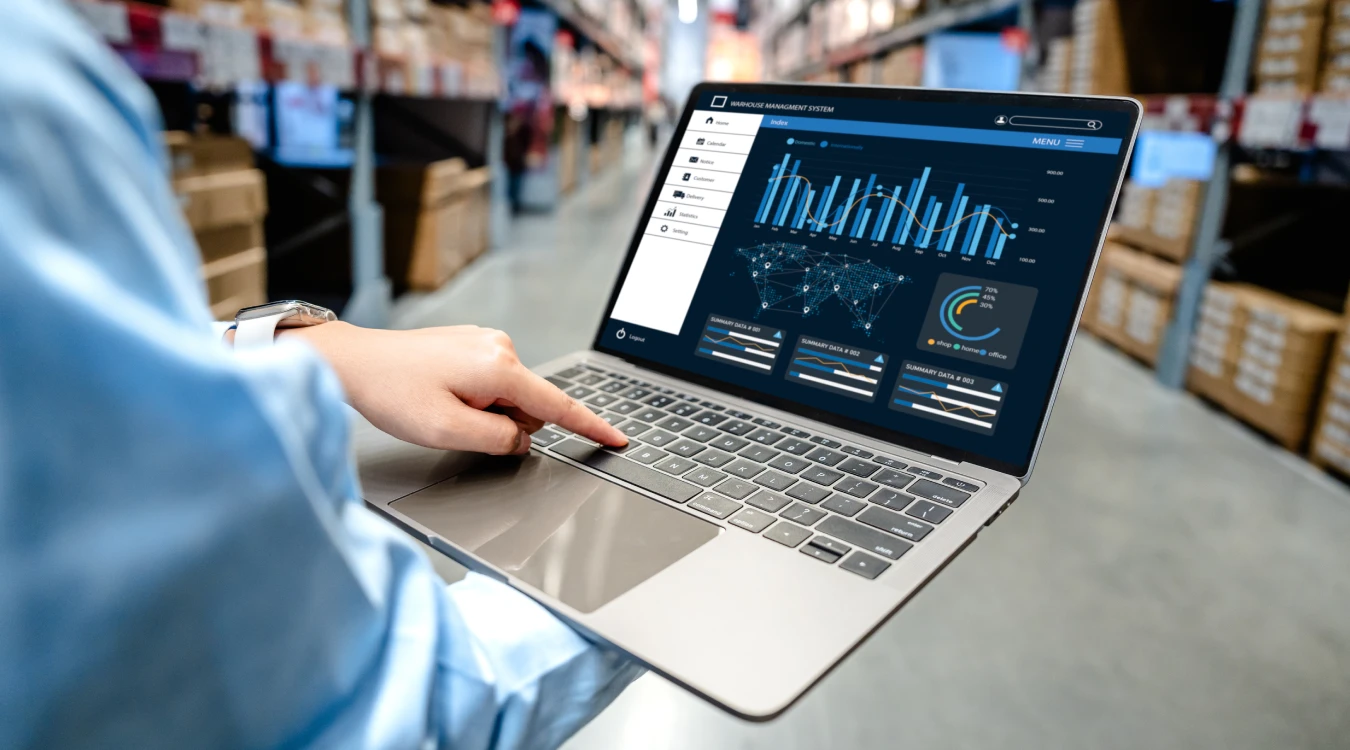Warehouse worker checking real-time WMS inventory visibility dashboard on a laptop